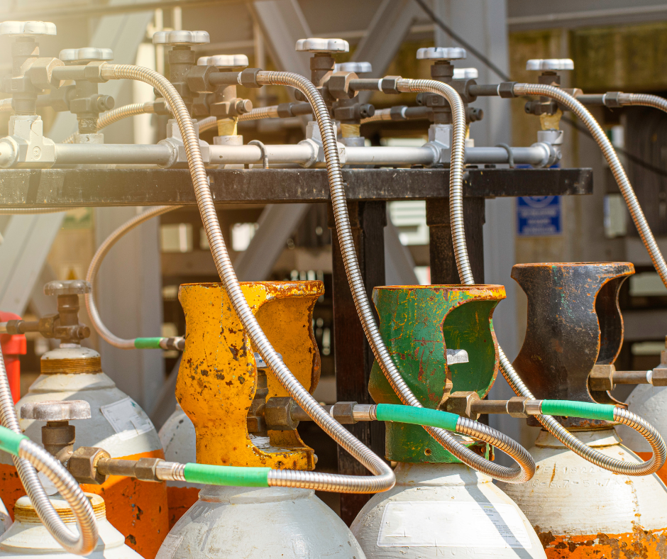 Several cylinder gas bottles lined up for refilling, with hoses connected and workers monitoring.
