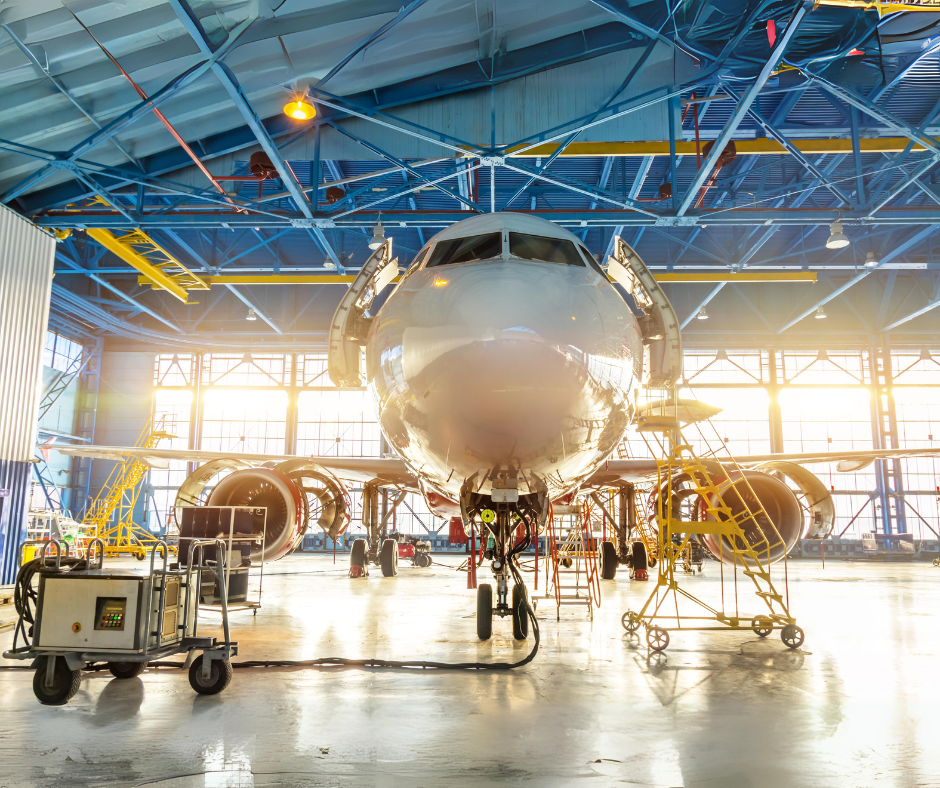 An aircraft in a hangar undergoing maintenance, with engine covers open and various maintenance equipment, including specialty gas cylinders, surrounding the plane. The image conveys a scene of technical expertise and aviation industry activity in a spacious, well-lit hangar.