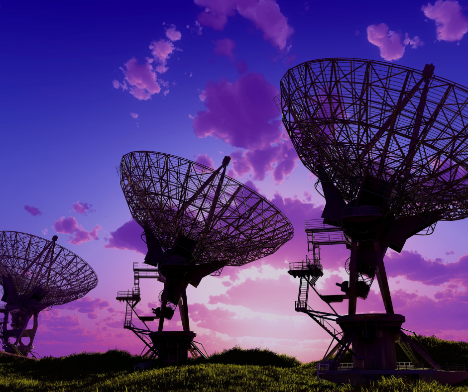 The image shows several large radio telescopes against a twilight sky. The telescopes have intricate mesh dishes pointed upwards, capturing signals from space. The sky is a vibrant purple and blue, with scattered clouds tinted by the setting or rising sun. The telescopes are situated on grassy ground, suggesting a remote location optimal for minimizing radio interference. The scene conveys a sense of exploration and the search for knowledge from the cosmos.