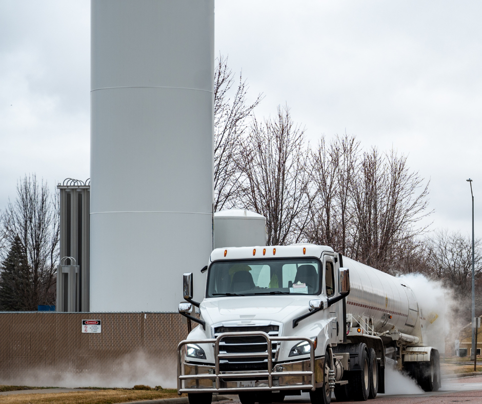 A white tanker truck delivering liquid oxygen to a large storage tank facility.