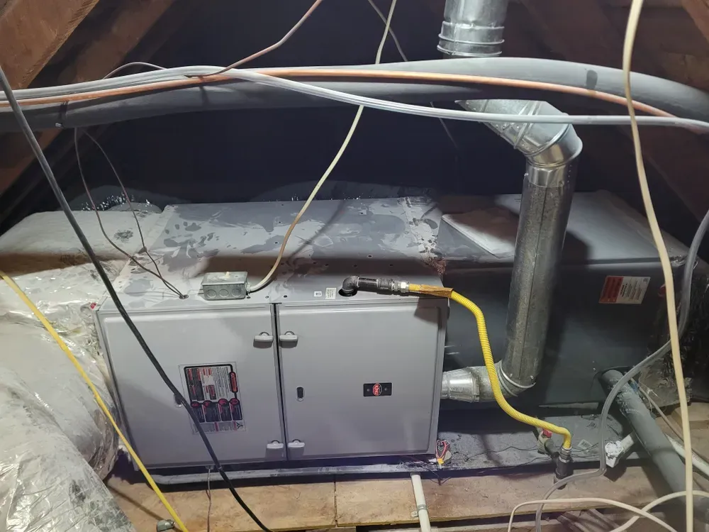 Furnace and HVAC unit in an attic, with ducts, wiring, and a yellow gas line.