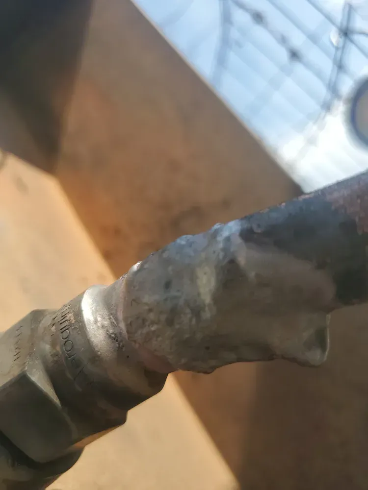 Close-up of a metal pipe fitting with a blob of shiny silver material.