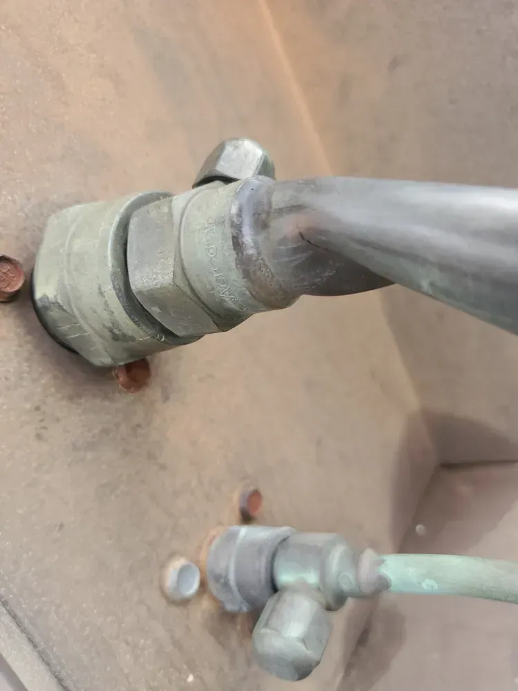 Close-up of metal pipes and fittings on a dusty brown surface. Copper-colored pipes and tarnished brass fittings.