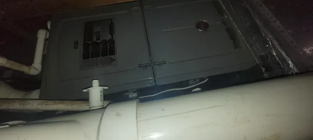 HVAC unit in an attic with white pipes and ductwork.