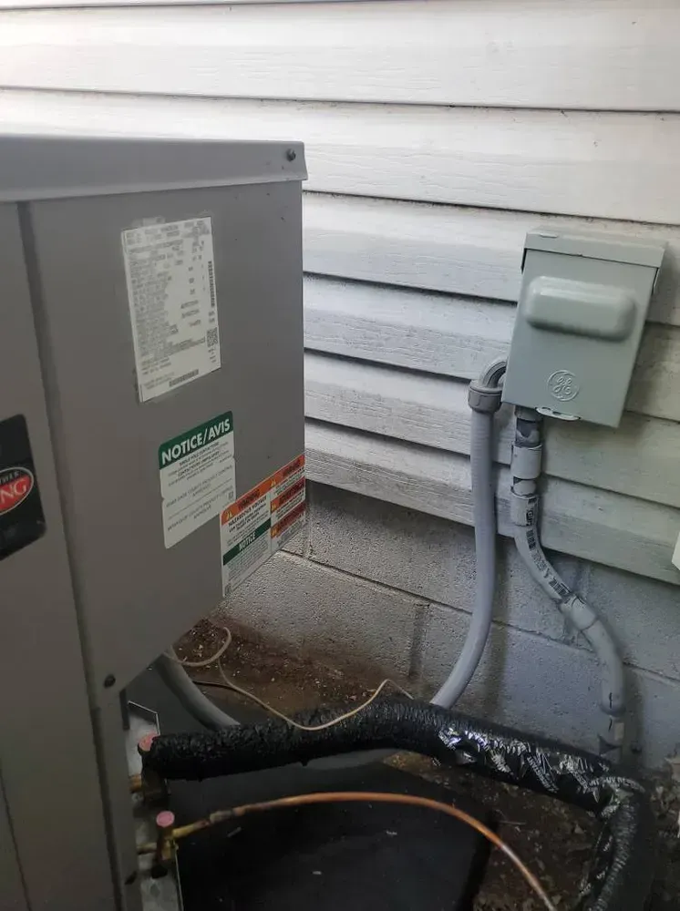 Air conditioner unit next to a light gray electrical box on a light gray siding wall.