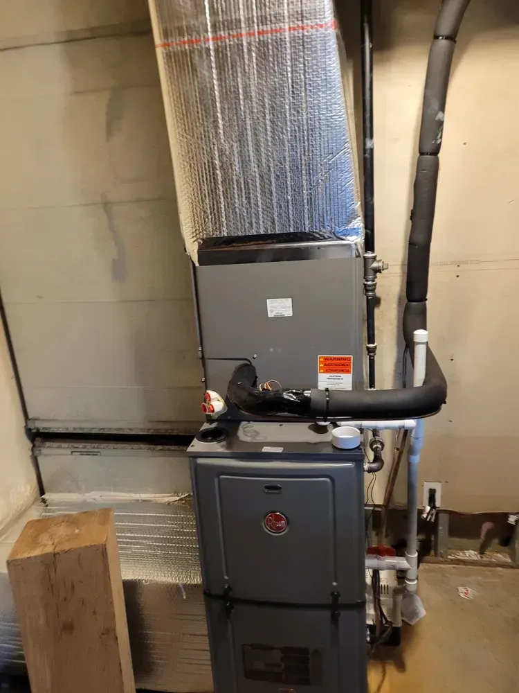 A Rheem furnace in a utility room. Gray metal unit with insulated ductwork.