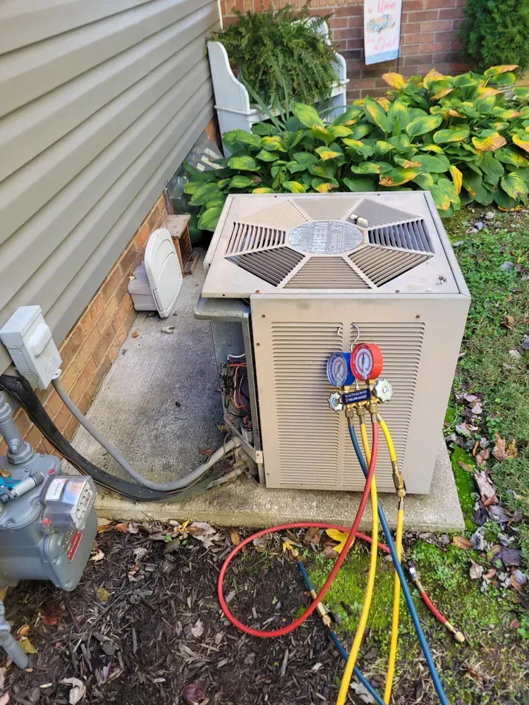 Air conditioning unit with gauges, connected to hoses, outdoors near a house.