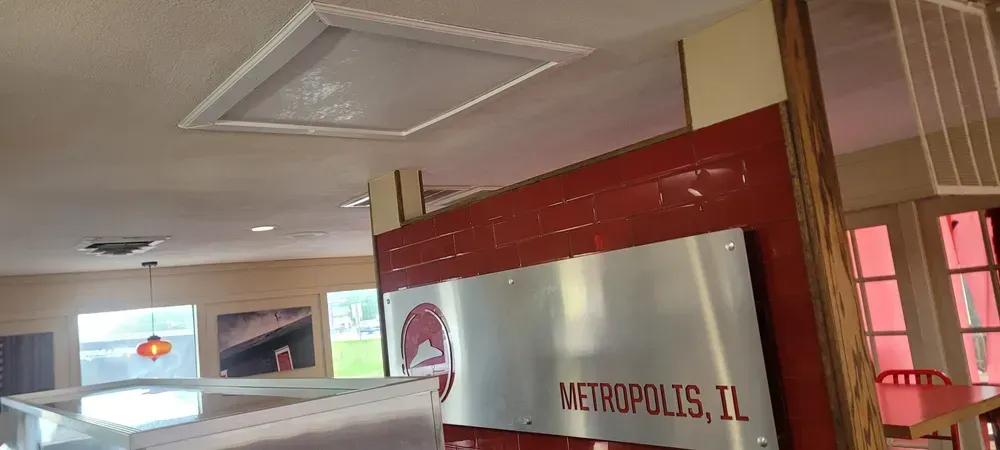 Sign for Metropolis, IL, in a room with a window, ceiling access, and a decorative light.