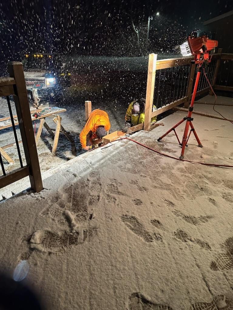 A man is kneeling in the snow on a construction site at night.