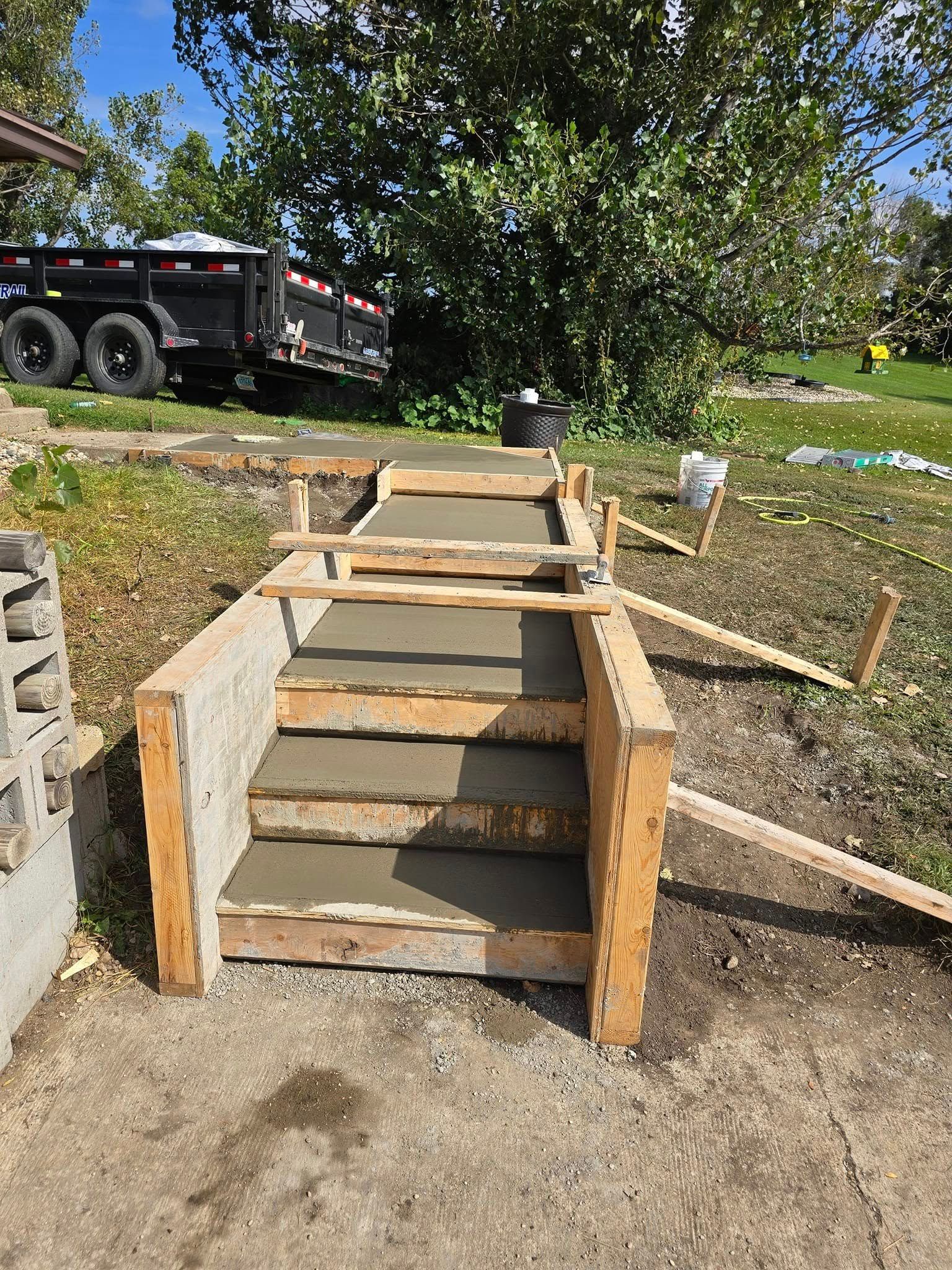 A concrete staircase is being built in a yard with a dumpster in the background.