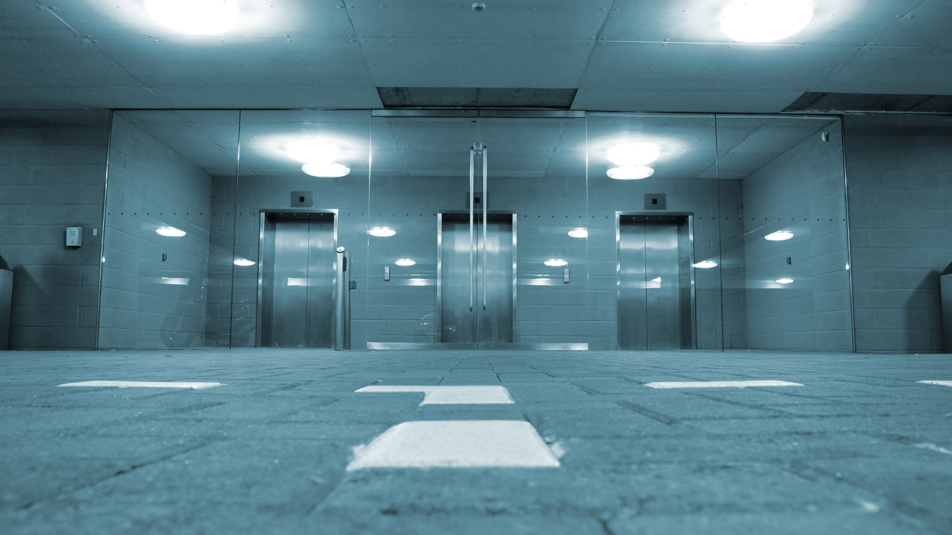 A hallway with two elevators and arrows on the floor.