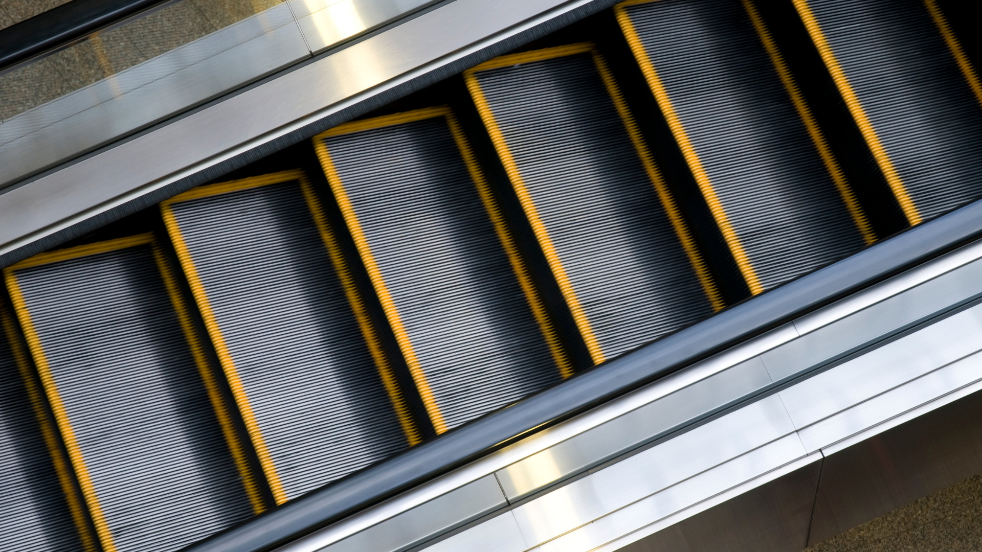 A close up of an escalator with yellow handrails.