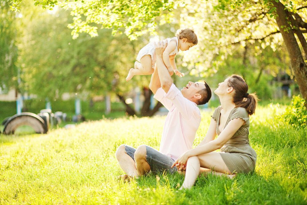 A family is sitting in the grass holding a baby in the air.