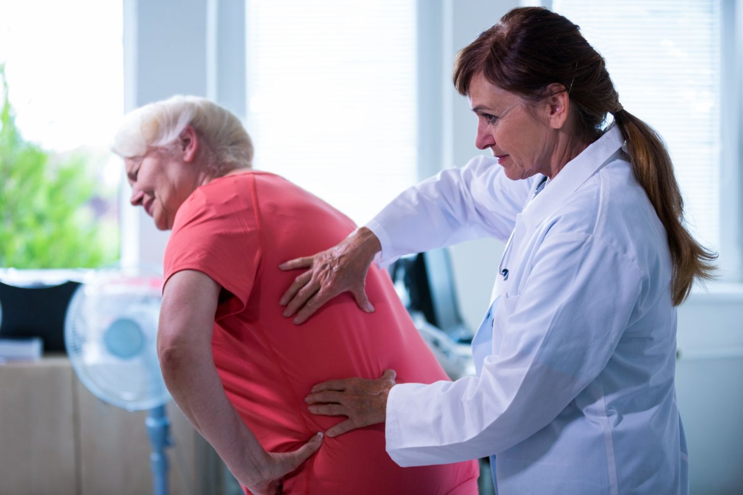 A doctor is examining an older woman 's back in a hospital.