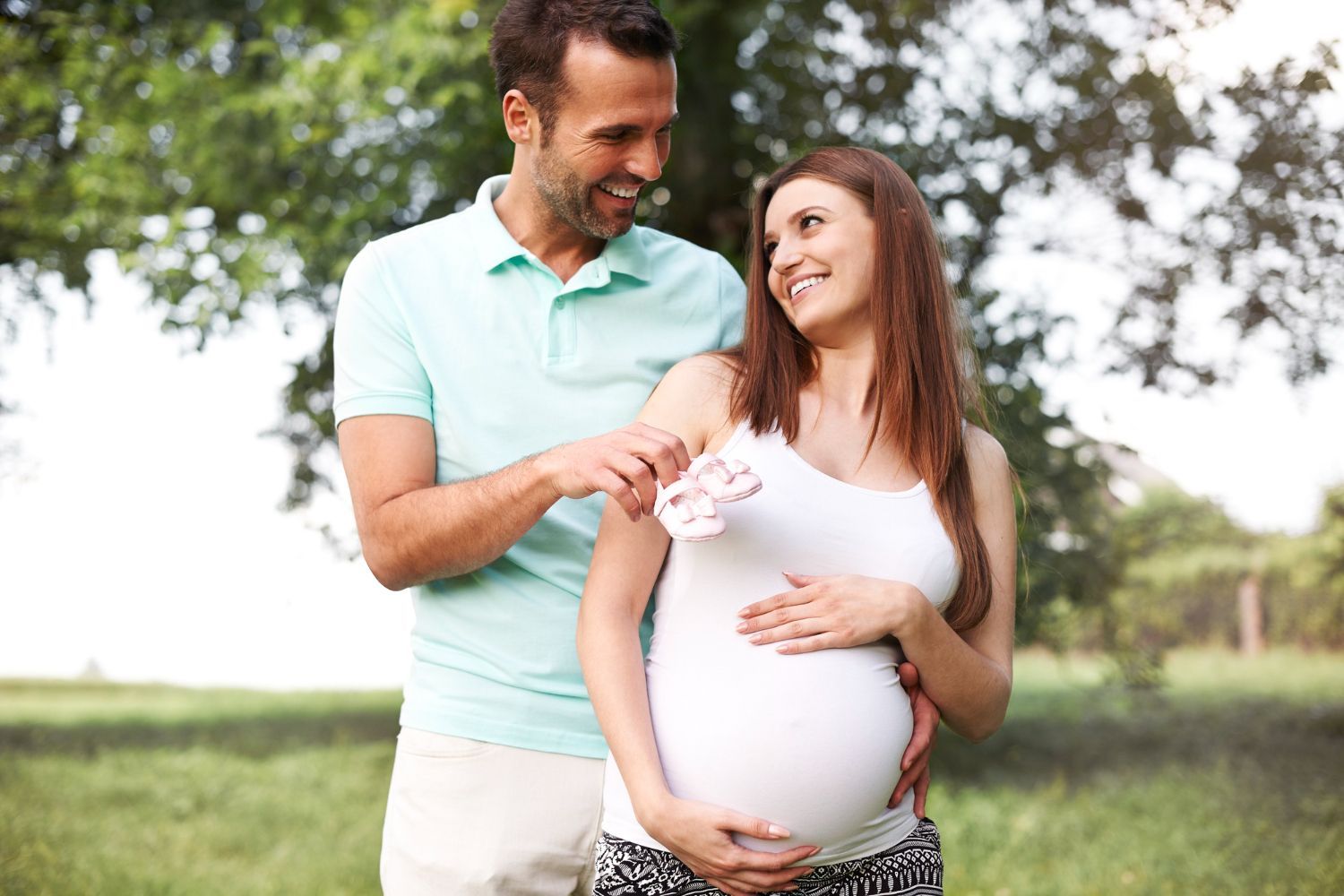 A man is holding a pair of baby shoes next to a pregnant woman.