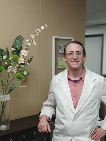 a man in a lab coat is standing in front of a vase of flowers .