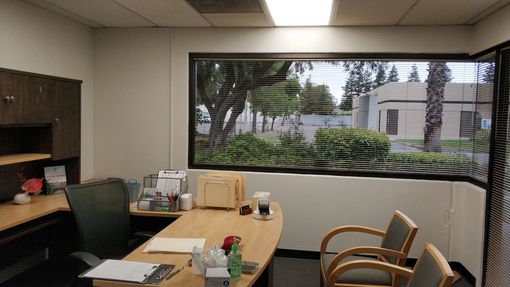 an office with a desk and chairs and a window with blinds