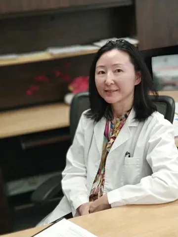 a woman in a white lab coat is sitting at a desk .