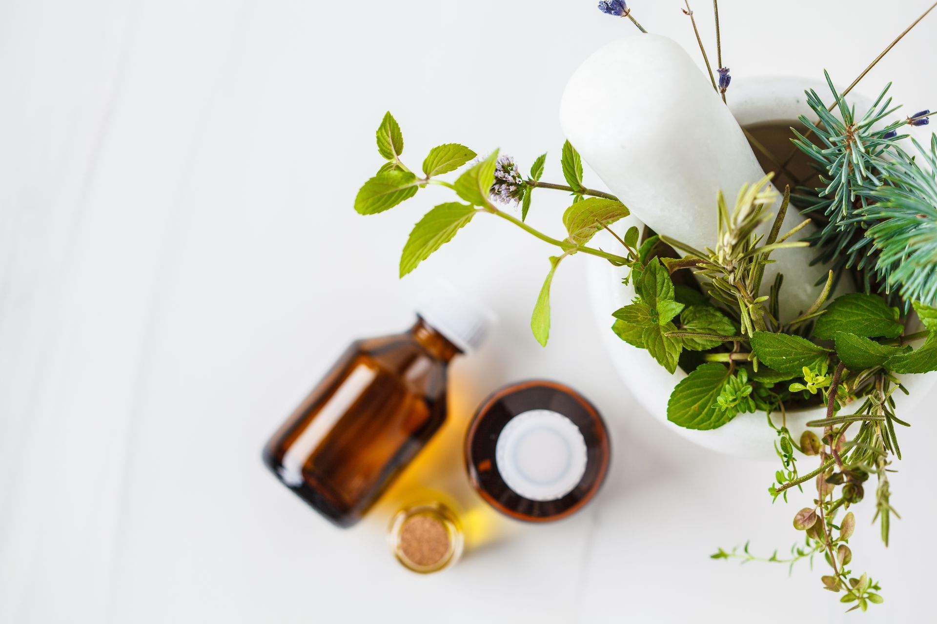 White mortar and pestle with herbs, brown bottles on white surface, natural remedy concept.