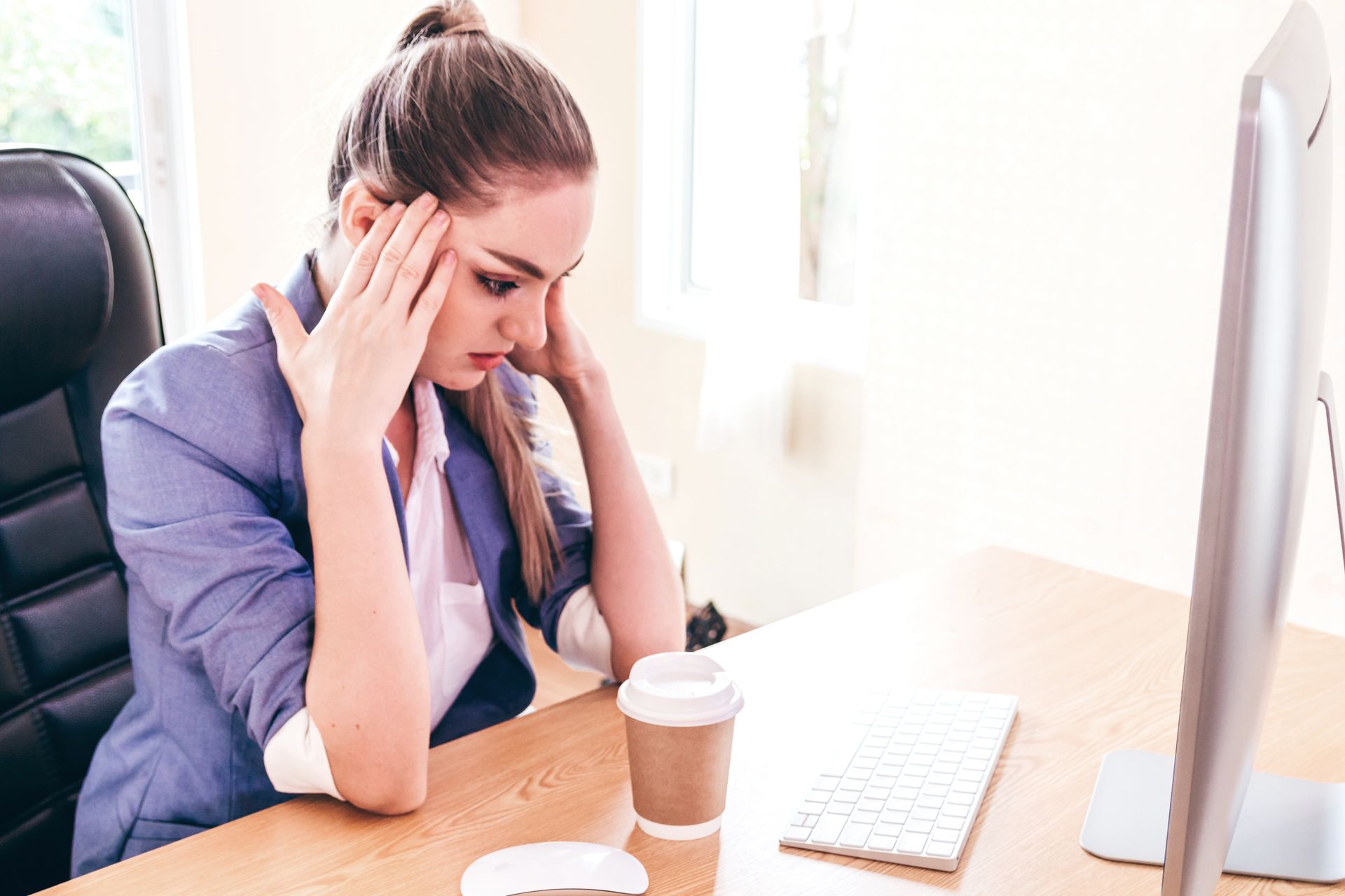 Woman with hands on head, looking stressed at a desk in front of a computer.