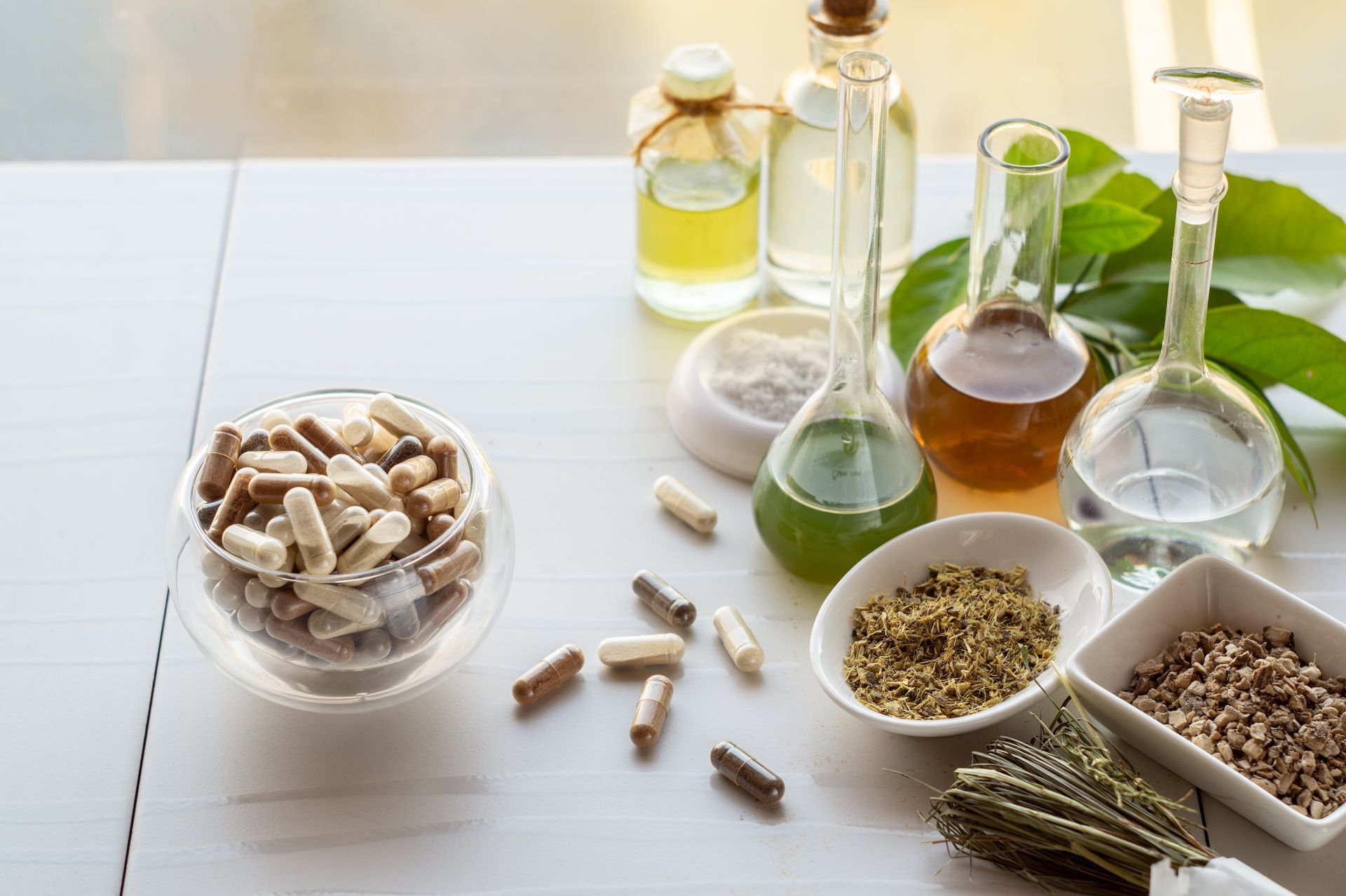 A table topped with bowls of pills , bottles of oil , beakers and leaves.
