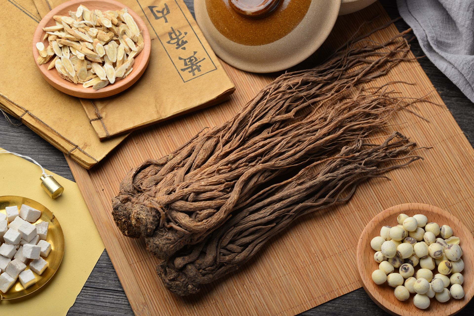 Dried herbal roots and ingredients on a table, with bowls and a book nearby.