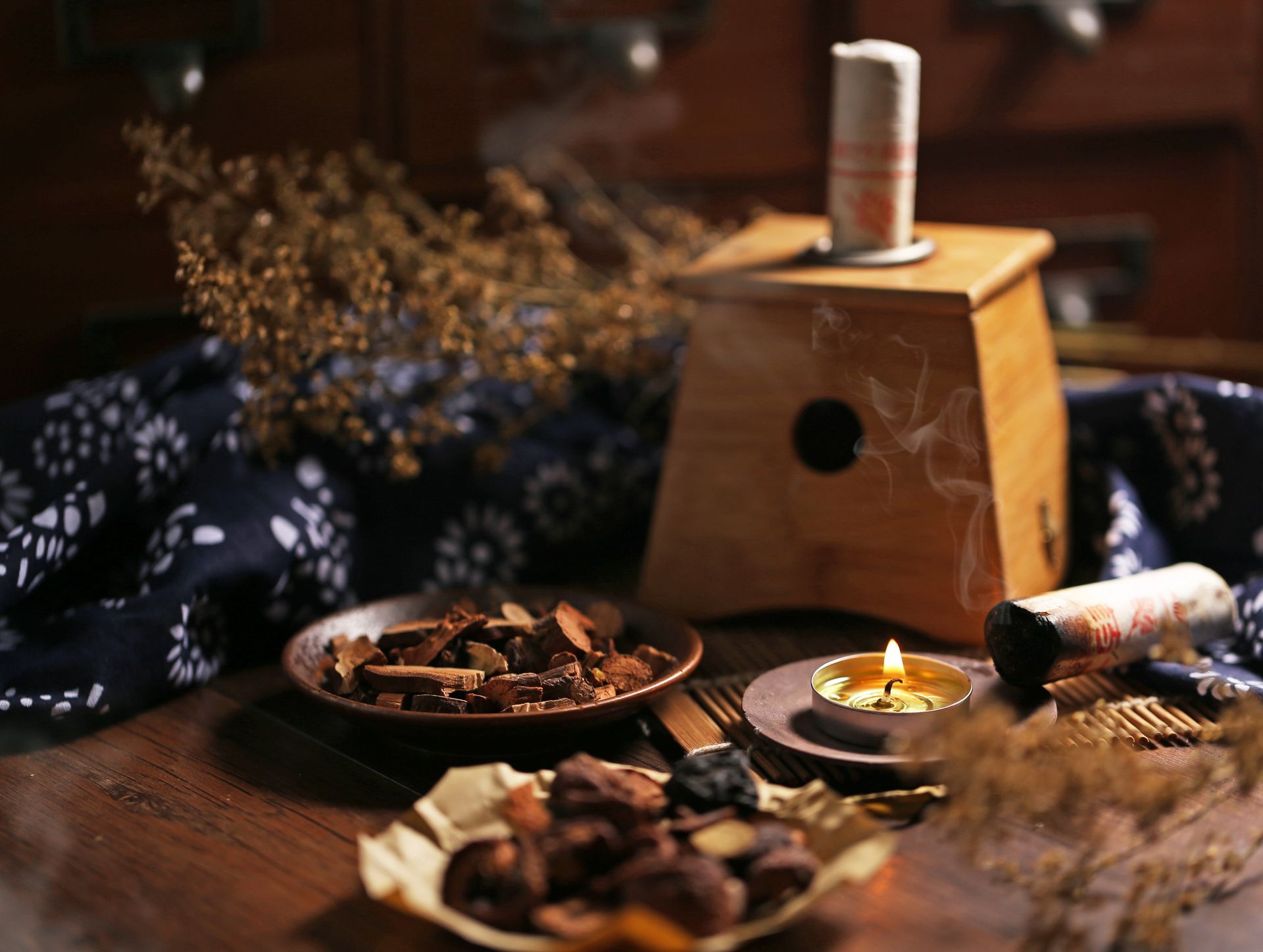 Wooden moxibustion box with smoke, herbs, and small candle on a table.