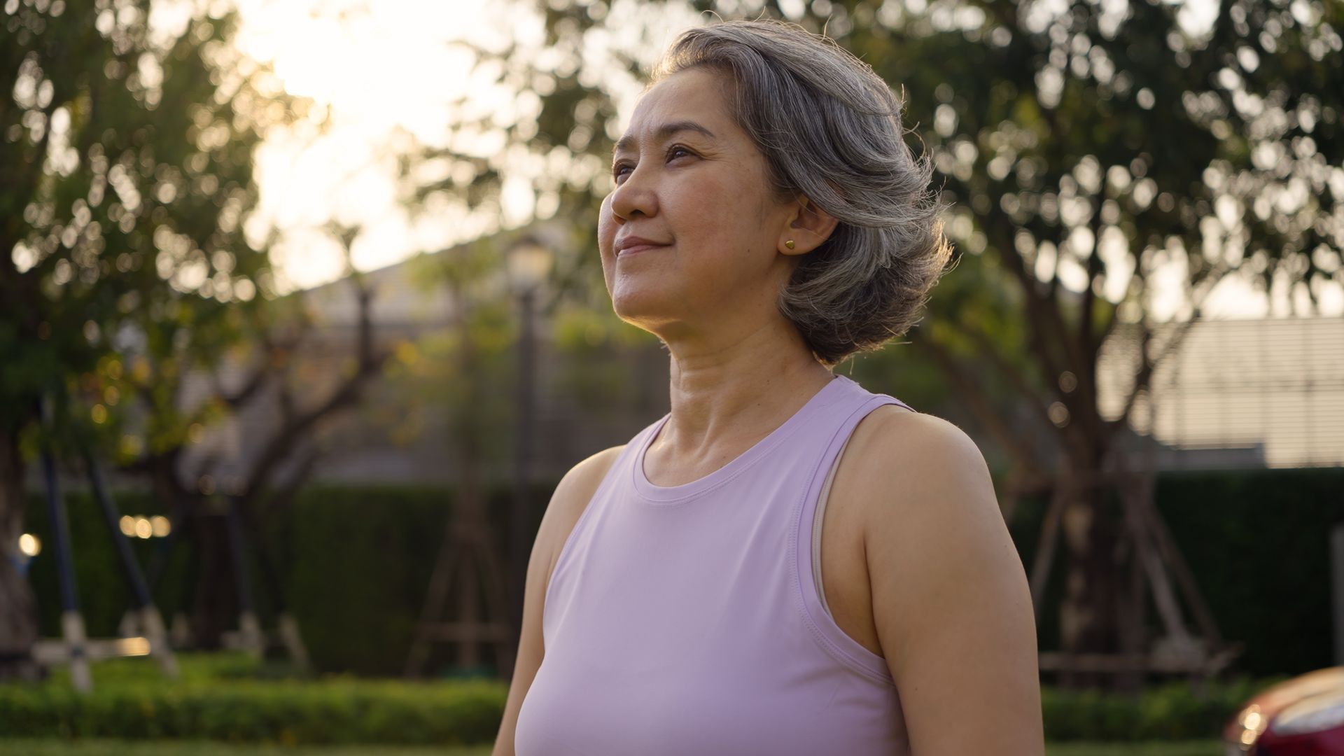 Woman in a lavender tank top standing outdoors at sunset, looking off to the side.