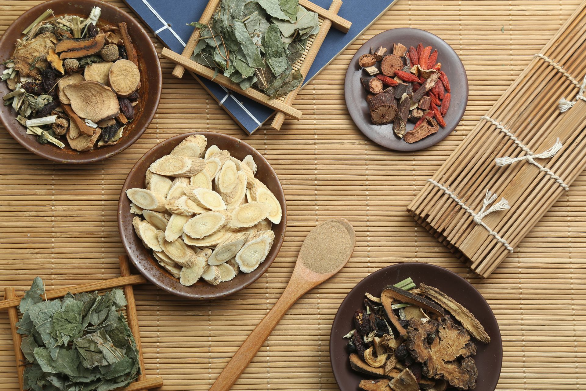 A wooden table topped with bowls of dried herbs and a wooden spoon.