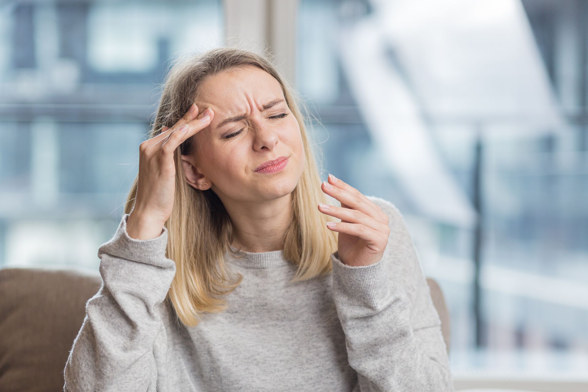 A woman is sitting on a couch with a headache.