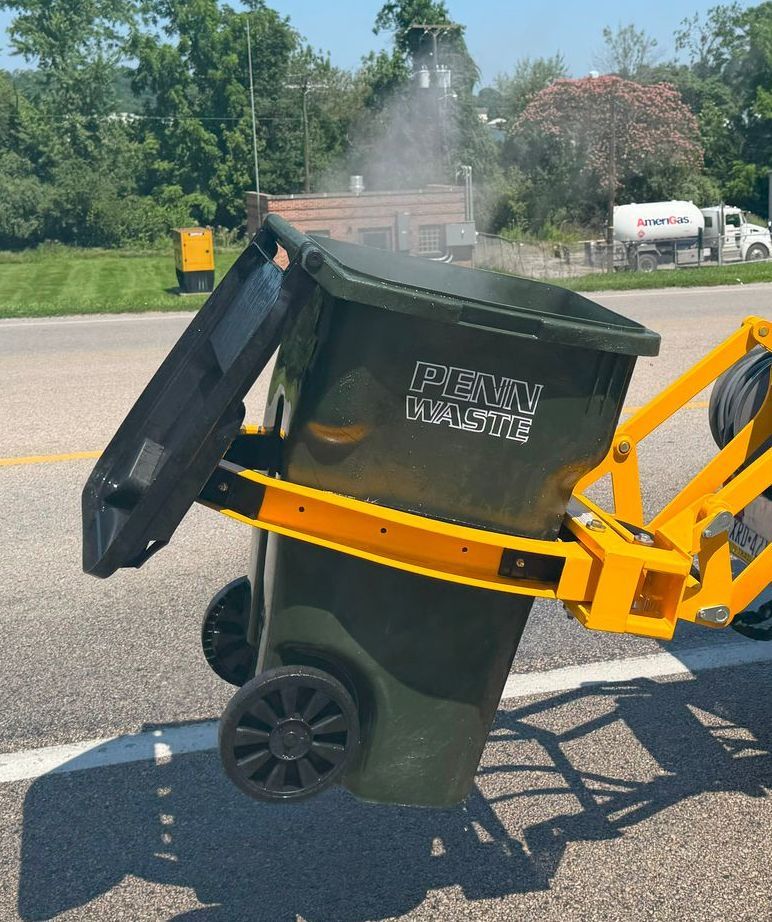 A man and a little girl are putting trash into a green trash can.