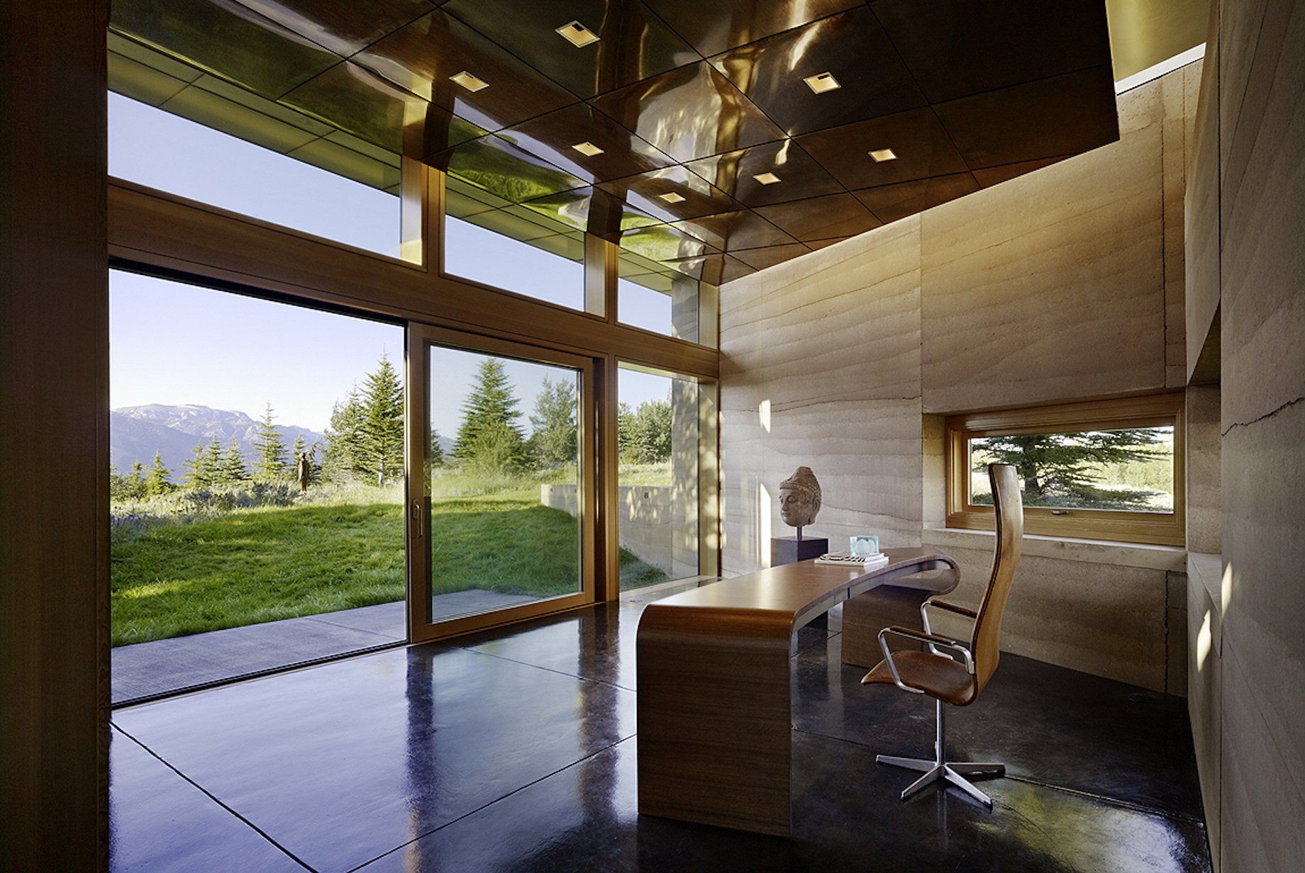 modern office with rammed earth SIREWALLs, a desk, reflective ceiling and large windows looking out to green mountain view
