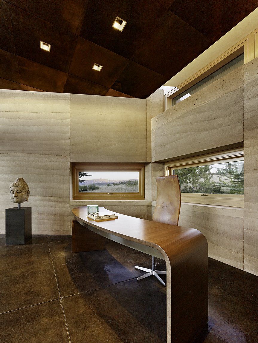 Office with rammed earth SIREWALL, a desk and a Buddha head sculpture