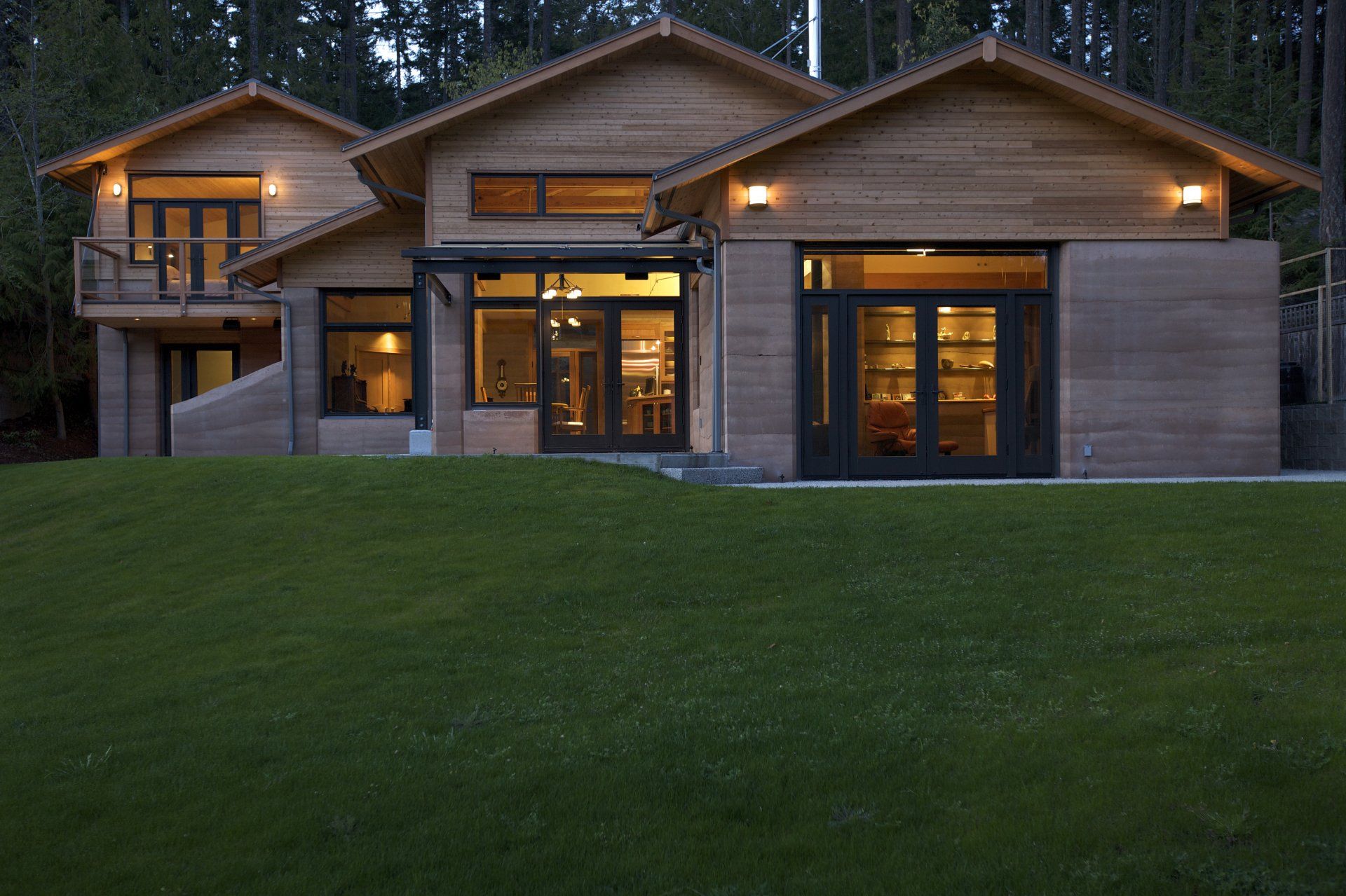 rammed earth home at dusk with lights on and green grassy hill