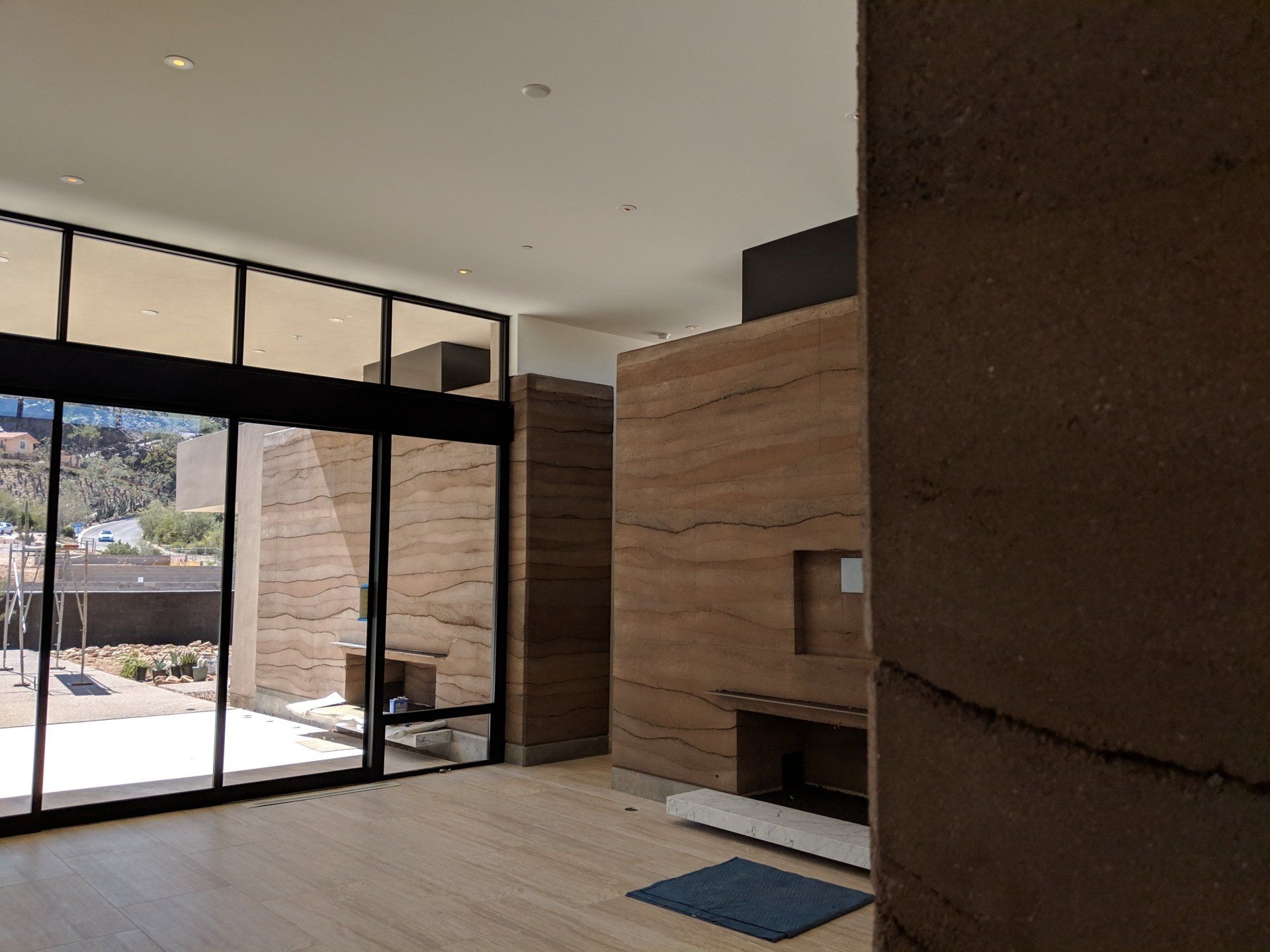 Living room with two rammed earth fireplaces, one indoors, and one outdoors -separated by floor-to-ceiling  glass wall.