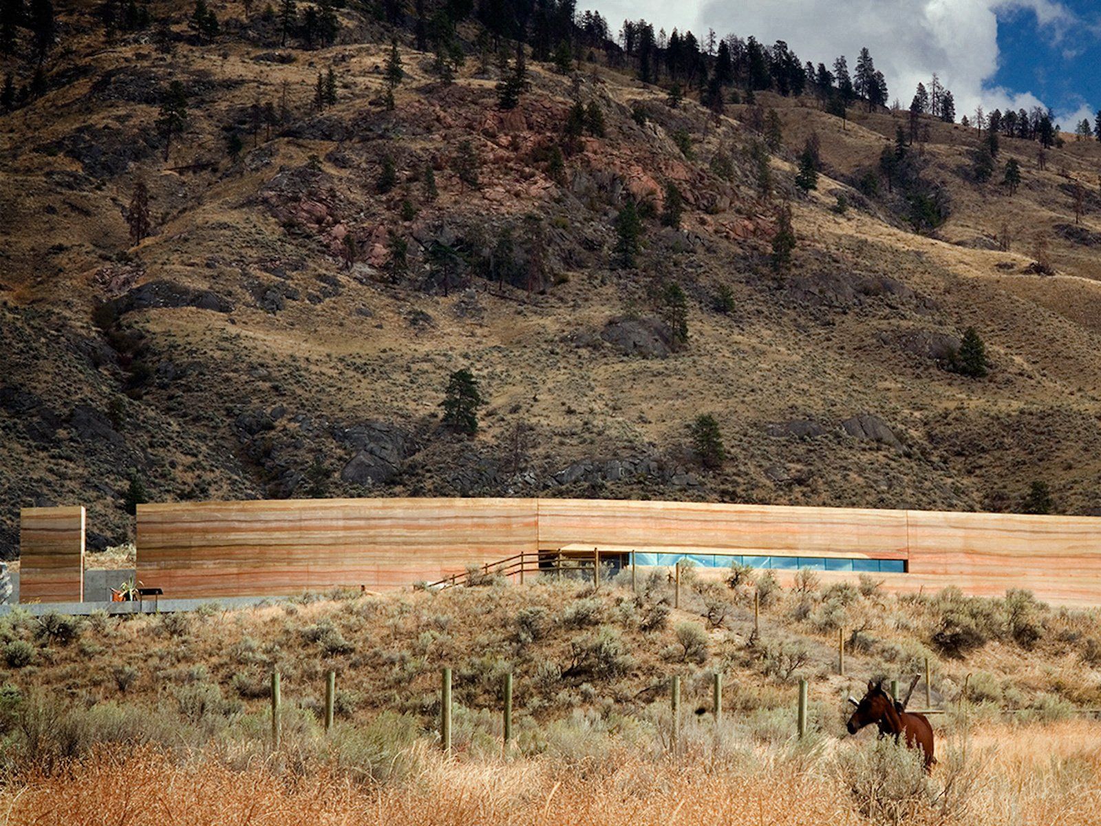 rammed earth SIREWALL building set in the desert with mountains and one horse