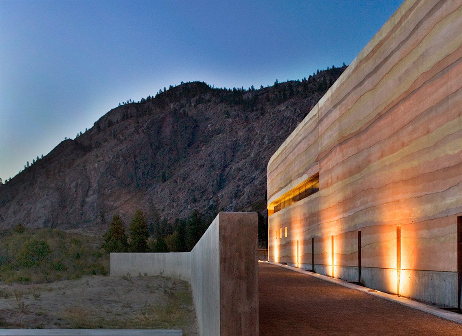nk mip wall  at dusk with lights going up the rammed earth SIREWALL, desert hill in background