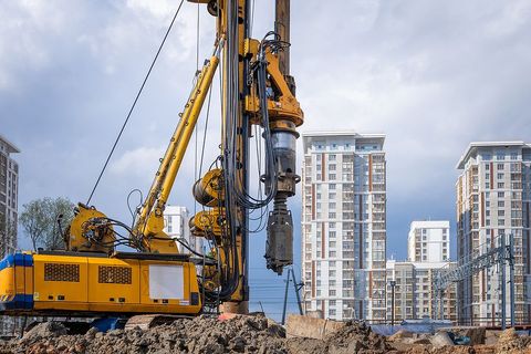 a yellow crane is working on a construction site with buildings in the background .