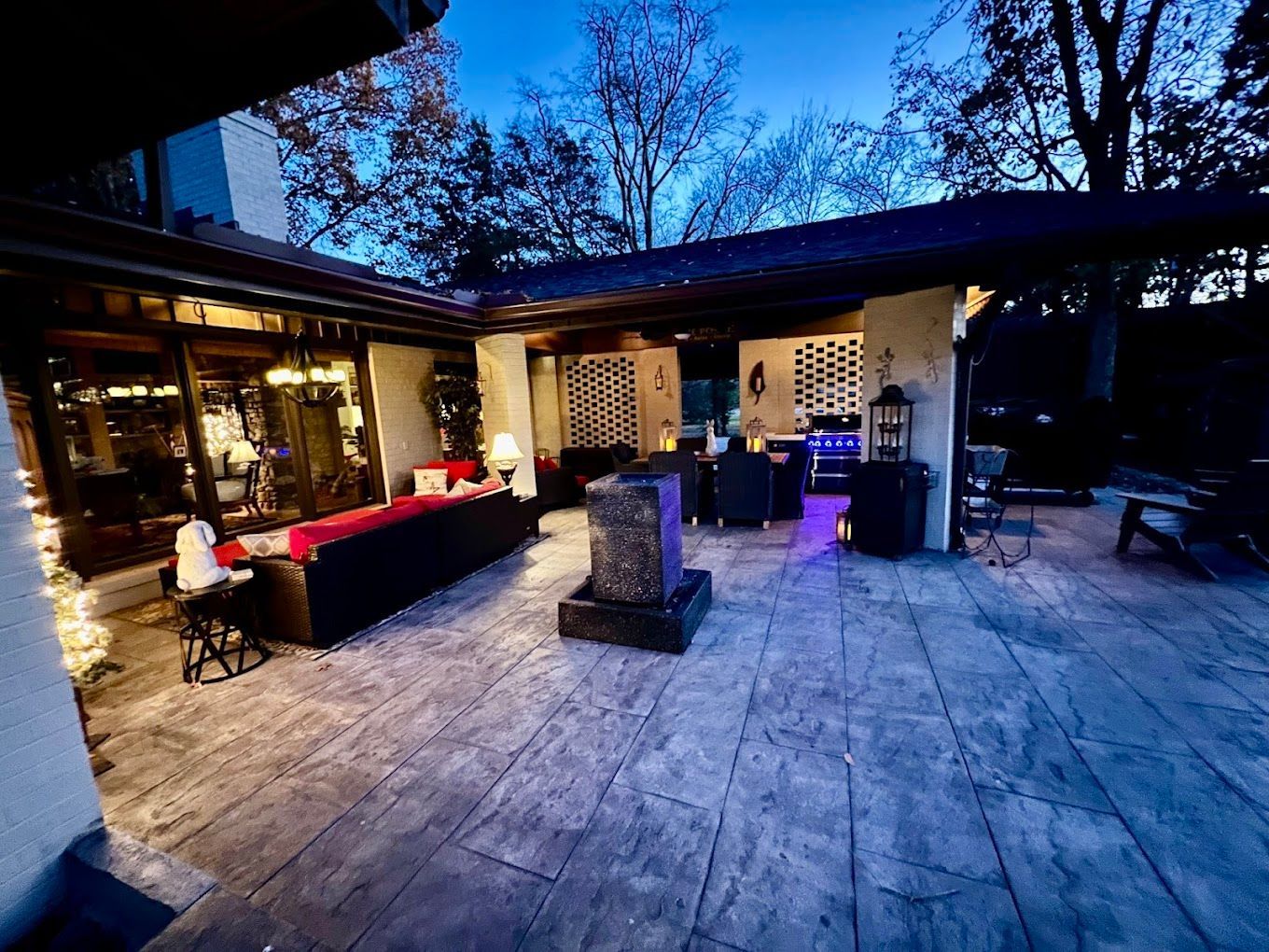 A large stamped patio with a lot of furniture and a fountain at night.
