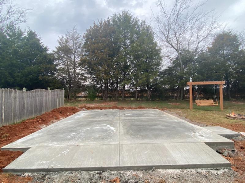 A concrete driveway is being built in a backyard with trees in the background.