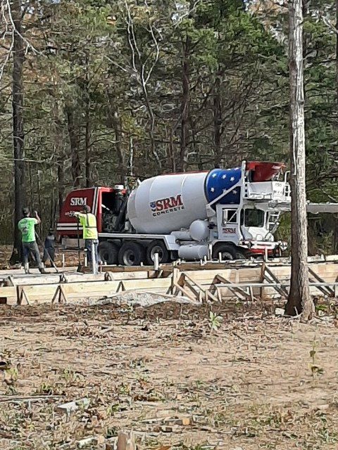 A concrete mixer truck is driving down a dirt road.