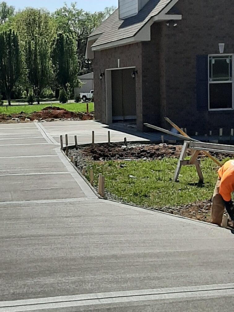 A man is working on a concrete driveway in front of a house.