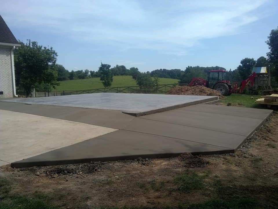 A concrete driveway is being built in a backyard with a tractor in the background.