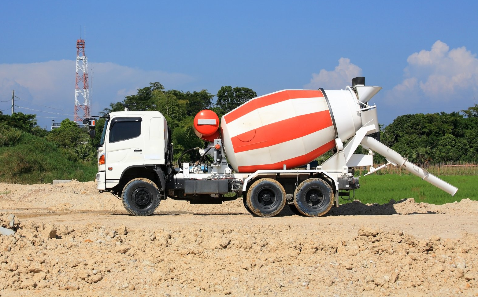 A concrete mixer truck is driving down a dirt road.