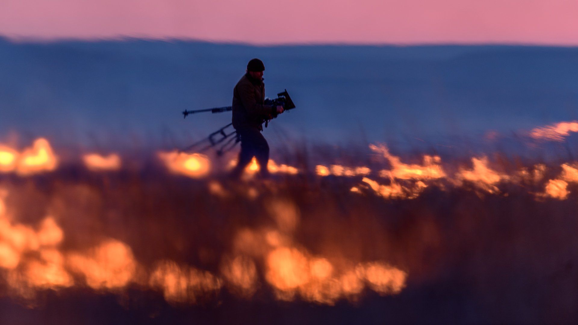 man walking through prairie on fire
