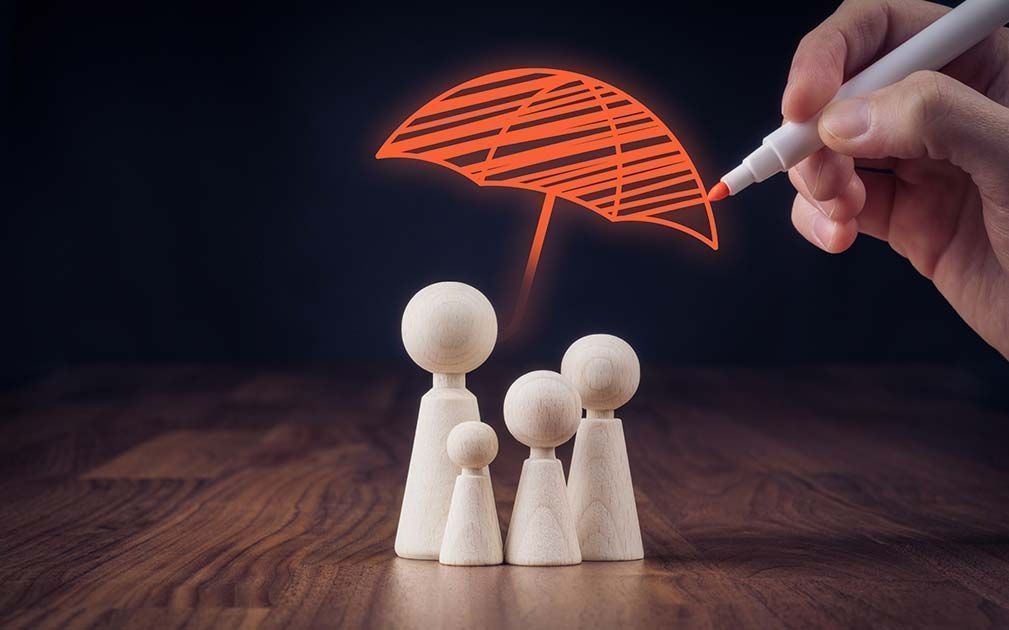 Wooden family figurines under a drawn orange umbrella, with a hand holding a pen.
