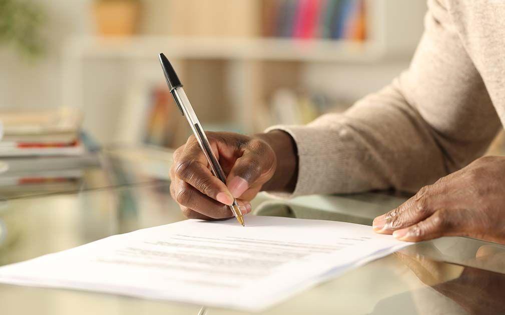 Person writing on a white paper with a pen, indoors.