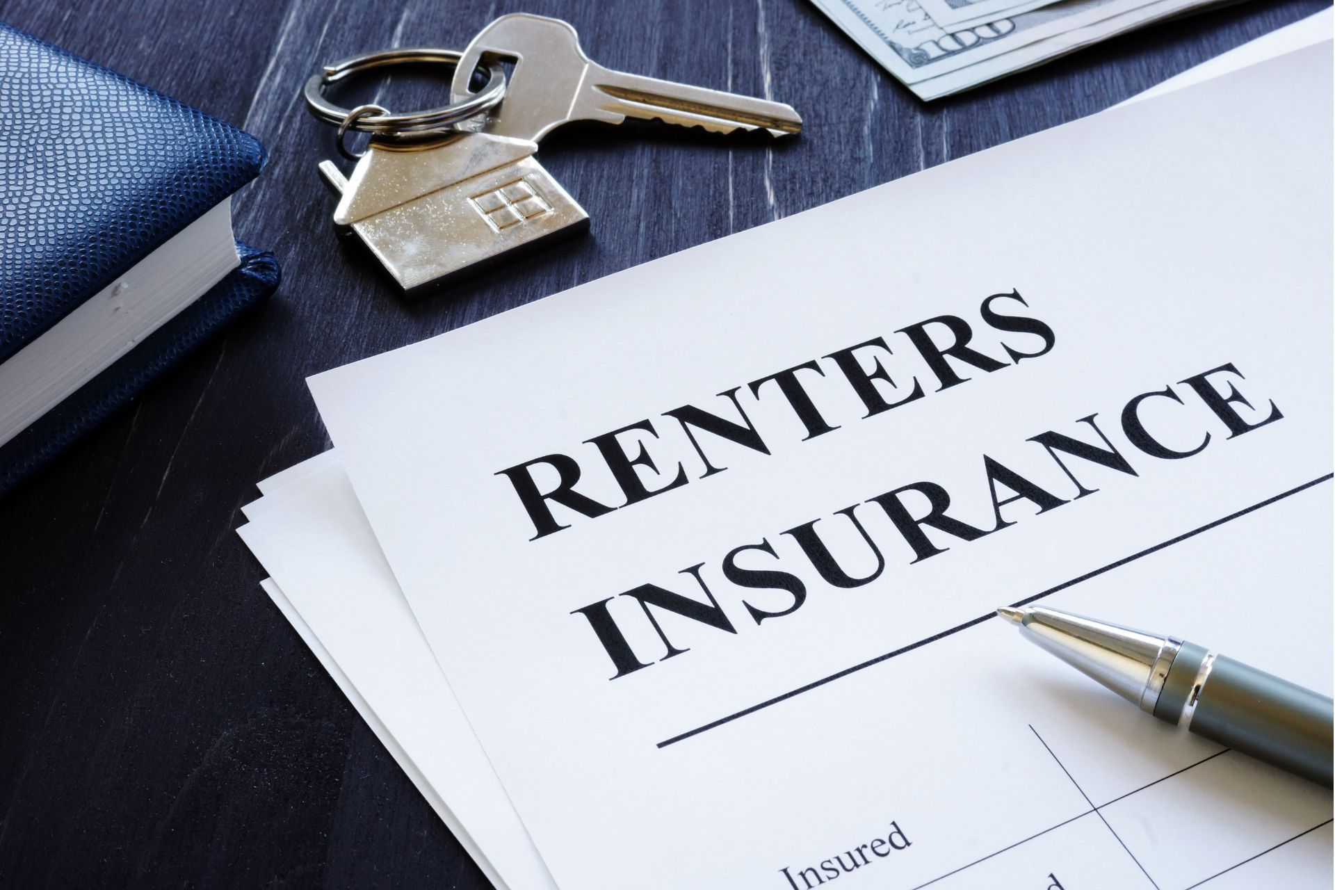 Renters insurance document with keys, money, and pen on a dark surface.