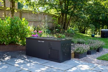 Black outdoor storage bench with flowers on a sunny stone patio in a garden