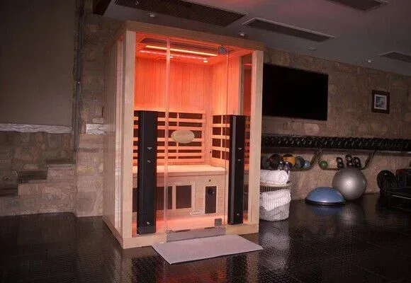 Orange-lit glass sauna room in a spa lounge with stone walls and exercise balls nearby